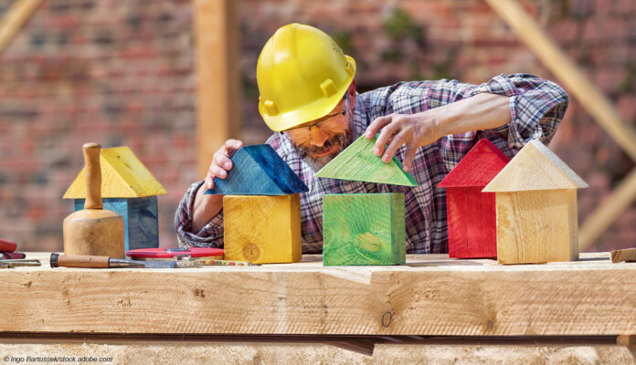 Hausbau Holz Bauarbeiter spielt mit Bauklötzen