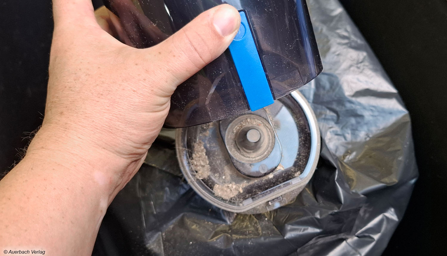 Der beutellose Schmutztank lässt sich per Druck auf die blaue Taste öffnen, sodass der Inhalt sauber und unkompliziert in die Mülltonne entleert werden kann